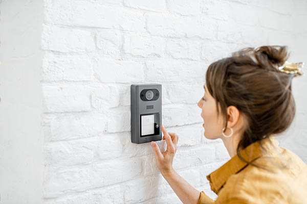 Woman ringing the bell on an intercom with a camera installed on a white brick wall